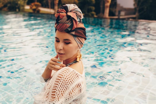 Woman with bright make up in bohemian outfit, turban, ethnic earrings, necklace and bracelets posing in swimming pool. photo