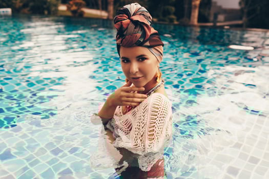 Woman with bright make up in bohemian outfit, turban, ethnic earrings, necklace and bracelets posing in swimming pool. photo