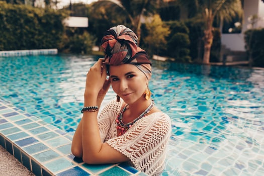 Woman with bright make up in bohemian outfit, turban, ethnic earrings, necklace and bracelets posing in swimming pool. photo
