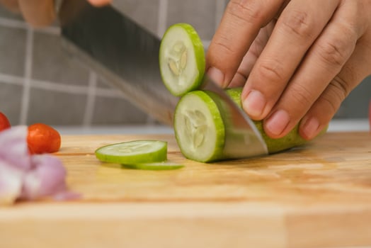 Female hand using a knife to slice cucumbers on a cutting board. Close-up. Woman with kitchen knife cutting cucumber at home. Preparing homemade food photo