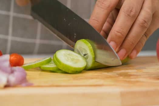 Female hand using a knife to slice cucumbers on a cutting board. Close-up. Woman with kitchen knife cutting cucumber at home. Preparing homemade food photo