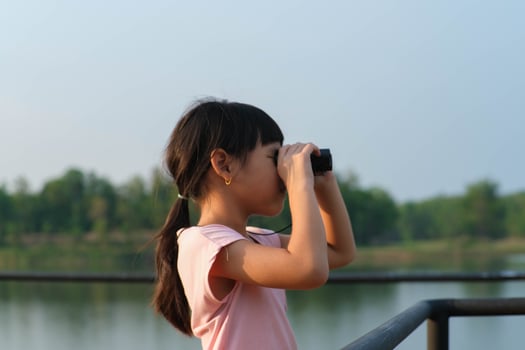 Little girl looking through binoculars at birds on the reservoir. Explore and adventure concept. Birdwatching photo
