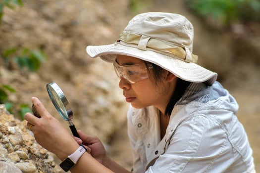 Female geologist using magnifying glass to examine and analyze rock, soil, sand in nature. Archaeologists explore the field. Environmental and ecology research. photo