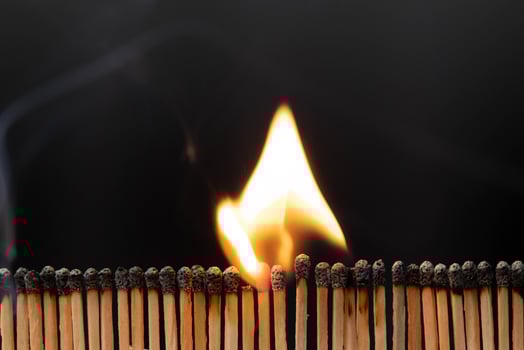 Rows of matches burning with flames close-up. View of the matches as they burn and smoke. Shot of igniting matches against black Background. photo