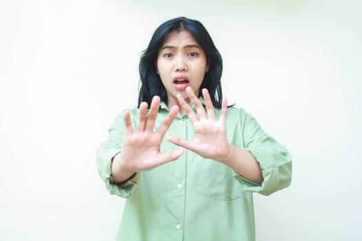 shocked dark hair asian woman reaching palms forward showing stop gesture wearing green oversized shirt looking at camera with scared face isolated on white background photo