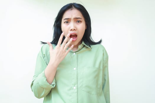 shocked dark hair asian woman looking at camera with open mouth showing wow expression and covering with hands wearing green oversized shirt isolated on white background photo