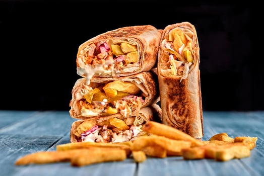 Shawarma chicken roll in a pita with fresh vegetables, cream sauce and french fries on wooden background. Selective focus photo