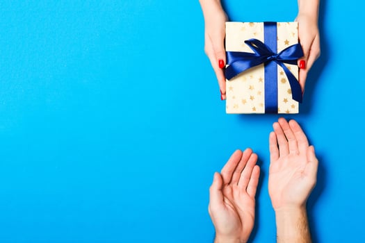 Top view of a gift in male and female hands on colorful background. Congratulation of each other concept. Close up photo