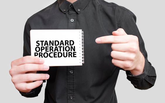 Businessman holding a white notepad with text STANDARD OPERATION PROCEDURE, business concept photo