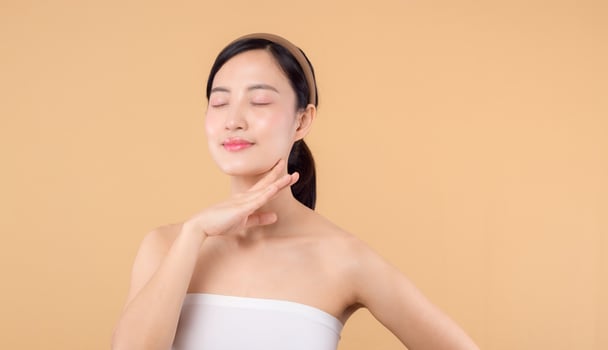 Beautiful girl asian model touching fresh glowing hydrated facial skin on beige background closeup. Beauty face young woman with natural makeup and healthy skin portrait. Skin care concept photo