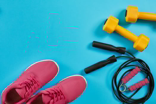 Athlete's set with female clothing, dumbbells and jump rope on bright blue background photo