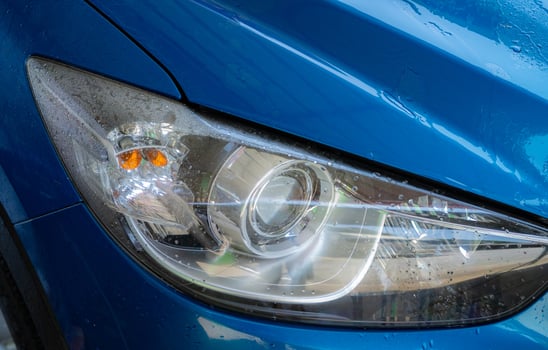 Closeup headlamp of blue car are washing with water. Car care service business concept. Car wash service. Car covered with drops of water after cleaning with high pressure water spray. Auto care. photo