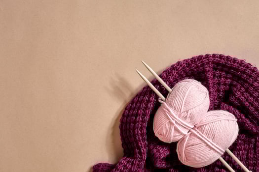 Two pink knitting yarn balls, knitting needles and and purple knitted plaid top view photo