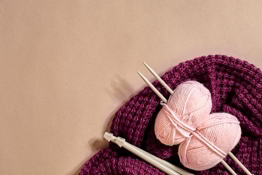 Two pink knitting yarn balls, knitting needles and and purple knitted plaid top view photo