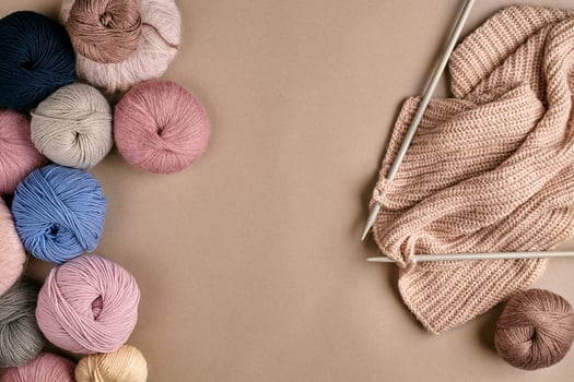 Set of colorful wool yarn and knitting on knitting needles on beige background. Top view photo