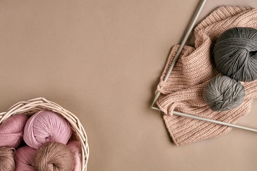 Balls of merino wool yarn, knitting on knitting needles on a beige surface. Top view photo