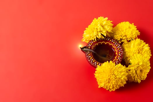 Happy Diwali and Kartika Deepam Festival Greetings - Colorful clay Deepam with yellow flowers on red background photo