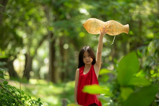 Little asian girl in red dress holding fishing equipment in the forest, Rural Thailand living life concept photo