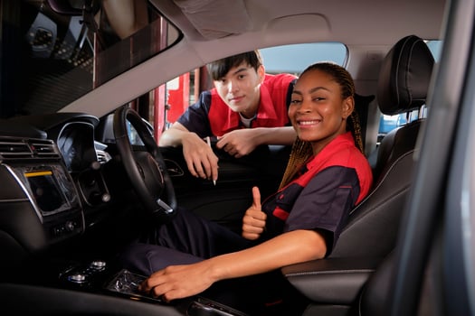 Young Black female automotive mechanic technician and partner check maintenance list in car interior at garage with smiles. Vehicle service fix and repair works, industrial occupation business jobs. photo