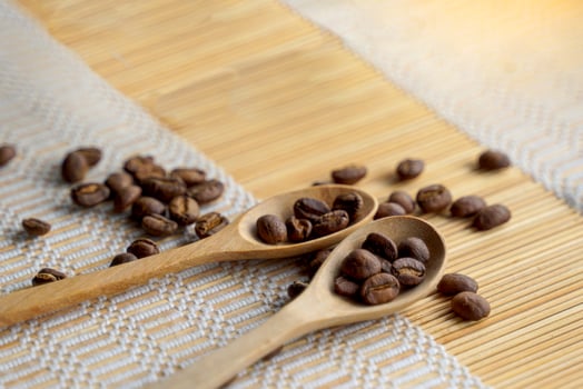 Roasted coffee beans in wooden spoon and spread on woven bamboo placemat. It is a medium roast with medium intensity coffee flavor. Slightly sweet and sour, suitable for both hot and cold coffee. photo