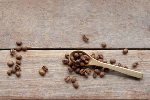 Roasted coffee beans in wooden spoon and spread on wooden table background. It is a medium roast with medium intensity coffee flavor. Slightly sweet and sour, suitable for both hot and cold coffee. photo