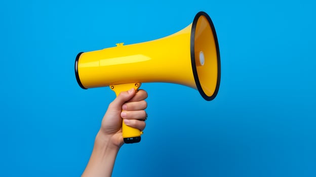 Hand Holding Yellow Megaphone Against Solid Blue Background photo