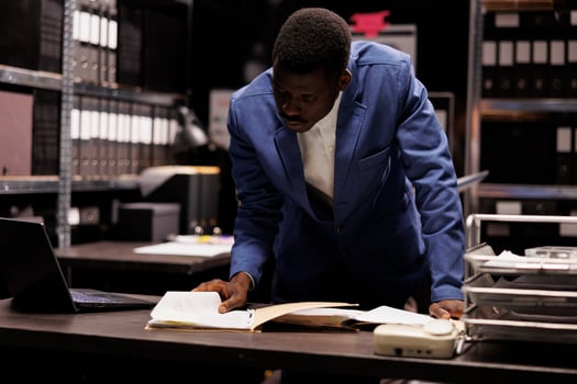African american manager working at accountancy report, analyzing administrative files in company repository. Businessman checking bureaucracy record, searching for management research photo
