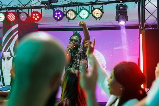 African american musician rapping on stage while crowd dancing at concert in nightclub. Cool dj singing in microphone while clubbers partying on dancefloor at performance in club photo