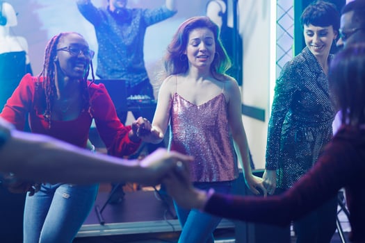 Carefree women holding hands and dancing together while partying in nightclub. Cheerful young diverse girlfriends clubbing and having fun on dancefloor, enjoying nightlife activity photo