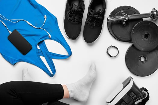 Flat lay gym equipment such as dumbbells, bottle of waters, smartphone with headphone, fitness bracelet and human legs in socks on white background. photo
