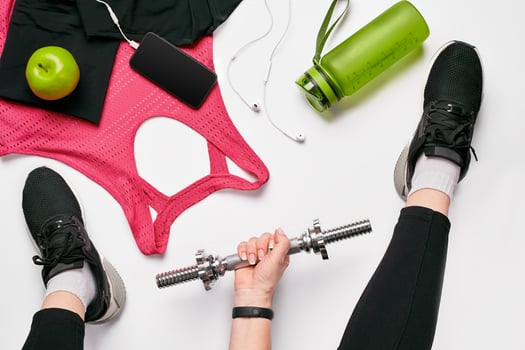 Girls legs wearing black trainers sitting on a mat surrounded by mobile phone, earphones, towel and a shaker in the fitness club. Top view. photo