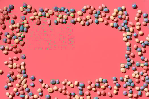 Multicolored glazed dragees are arranged in the form of a frame on a coral background. photo