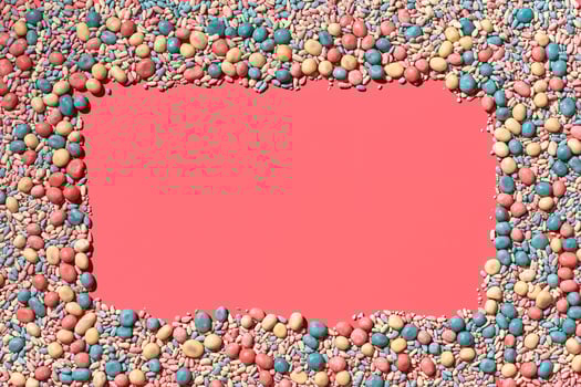 Multicolored glazed dragees are arranged in the form of a frame on a coral background. photo