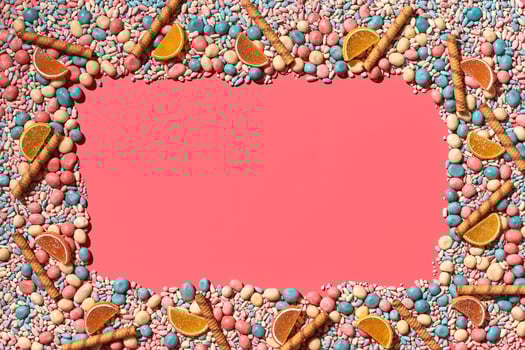 Multicolored glazed dragees and other sweets are arranged in the form of a frame on a coral background. photo