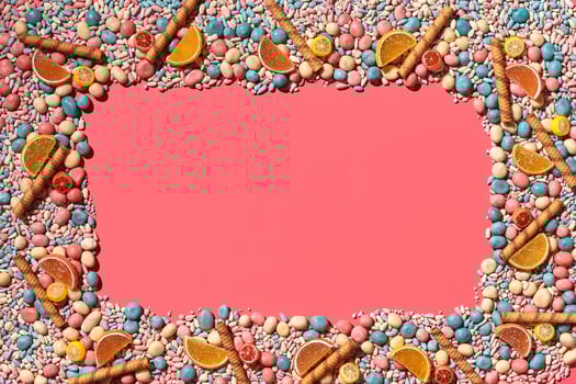 Multicolored glazed dragees and other sweets are arranged in the form of a frame on a coral background. photo