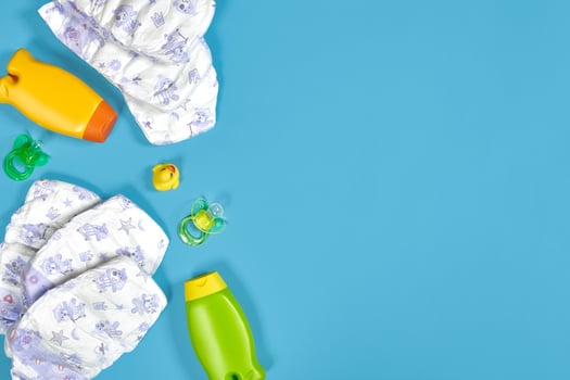 Baby care with bath set. Nipple, toy, diapers, shampoo on blue background top view mockup photo