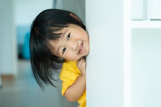 little asian children kid playing hide and seek standing next wall house, Adorable child having fun in the home. happy family have fun with kids, activity, learning, activity, game, meditation photo