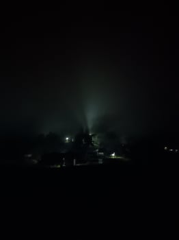 fir trees on meadow between hillsides with conifer forest in fog under the blue sky at night. spooky countryside scenery in full moon light photo