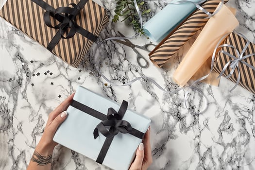 Hands of a woman are holding white paper gift box tied with black ribbon and bow against a marble background. Close-up, copy space, top view. photo