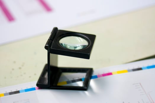 Magnifying glass inspecting printed sheets for sharpness and color accuracy, quality control workflow in prepress and publishing, highlighting detail, precision, and craftsmanship. photo