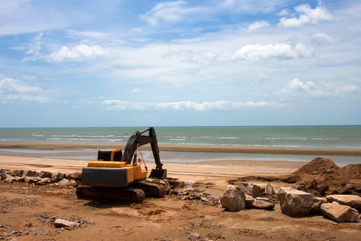 Heavy excavator working on sandy beach construction site under blue sky, concept of industrial work, development, and engineering. photo