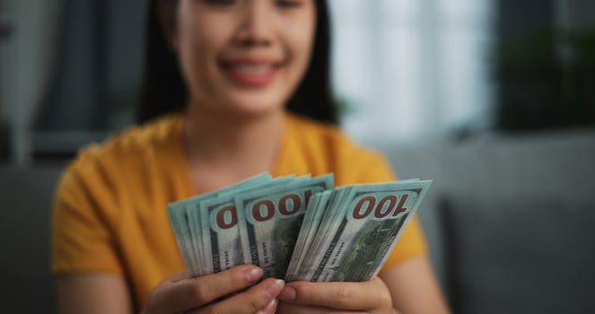 Portrait of young Asian woman enjoy counting cash dollars banknotes on sofa in the living room at home. photo