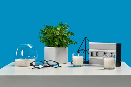 White table with candles on it and in a glass candlestick, greenery in pot, glasses, iron triangle, home decor element. Blue background. Close up photo