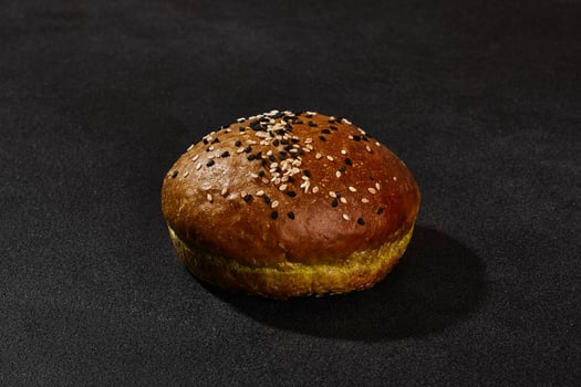 Fresh, baked, green bun sprinkled with sesame seeds against black background with copy space. Rural cuisine or bakery. Close-up photo