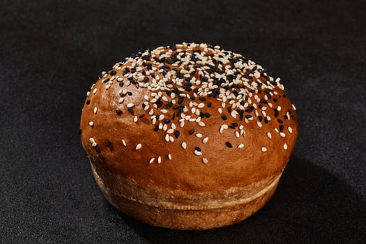 Fresh, delicious baked bun sprinkled with sesame seeds against black background with copy space. Rural cuisine or bakery. Close-up photo