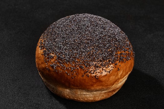 Fresh, yummy baked bun sprinkled with poppy seeds against black background with copy space. Rural cuisine or bakery. Close-up photo