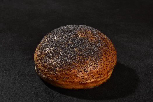 Fresh, delicious baked bun sprinkled with poppy seeds against black background with copy space. Rural cuisine or bakery. Close-up photo