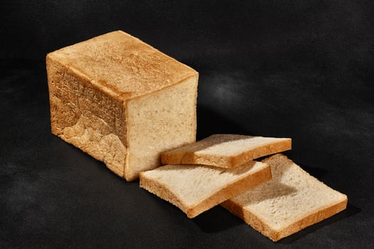Sliced loaf of fresh, palatable baked white bread against black background with copy space. Close-up photo