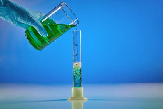 Hand in disposable glove is pouring green liquid from beaker into measuring cylinder, blue background. Coronavirus. Worldwide pandemic COVID-19 photo