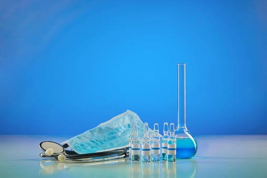 Medical flask with chemical reagent. Six ampoules with transparent liquid, mask and phonendoscope, blue background. Coronavirus, worldwide pandemic photo